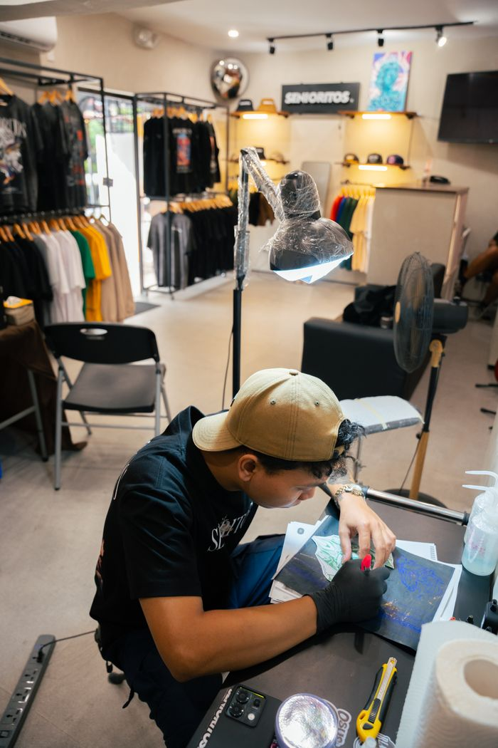 A focused tattoo artist working on a design in a trendy studio with clothing display.